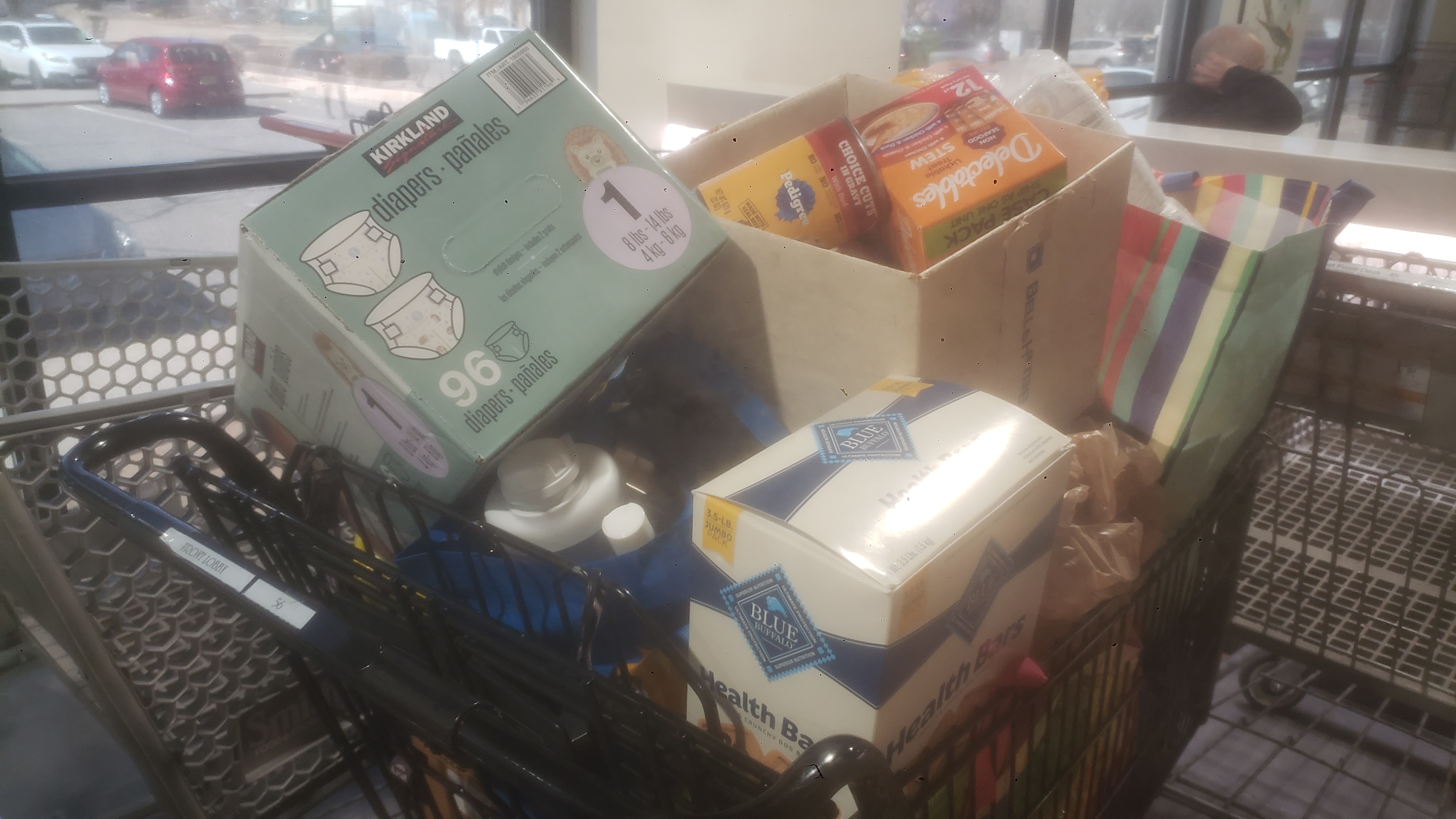 Shopping cart filled with pet food and a box of diapers.